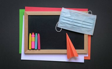 Siyah tahtanın üstünde yüz maskesi kağıt uçaklı renkli kağıtlar ve renkli pastel boyalarla. Düz yatıyordu.