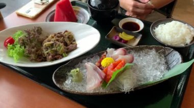 Japon mutfağı yemekleri, pirinçli sashimi tabağı, salata ve meyveler. Lokantada bir masada servis edildi..