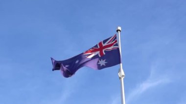 Avustralya bayrağı direkte sallanıyor, ağır çekimde. Mavi gökyüzüne karşı.