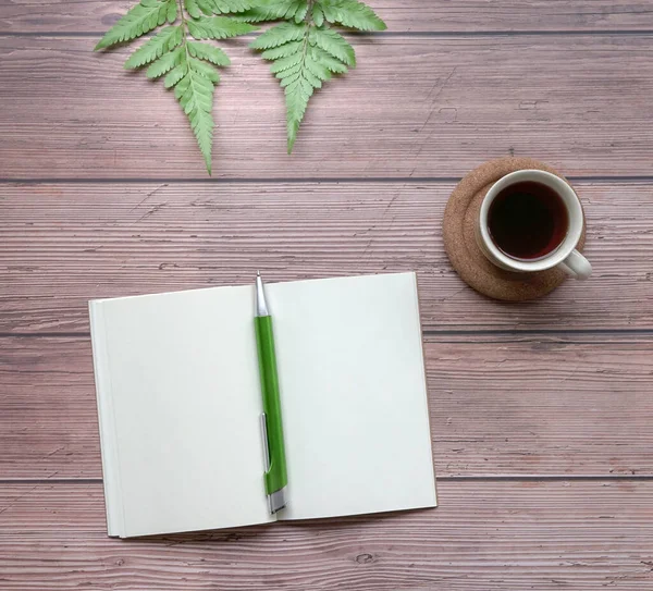 Open notepad with pen, coffee and green plants on wood table. Top view.