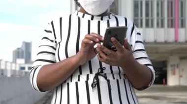 Asyalı iş kadını ayakta cep telefonunu okuyor. Açık hava, kentsel ortam.
