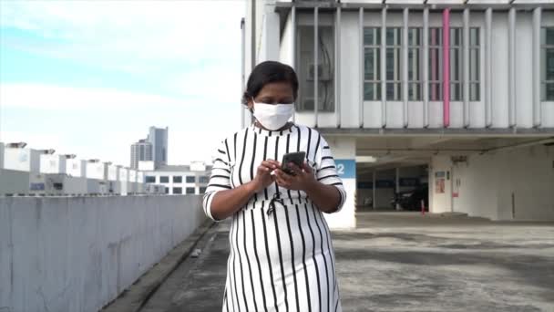 亚洲女商人 戴着口罩一边走路一边看手机 在办公大楼外面慢动作 — 图库视频影像