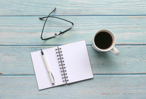 Mavi ahşap masanın üzerinde kalem, gözlük ve kahve bulunan not defterini aç. Üst görünüm.