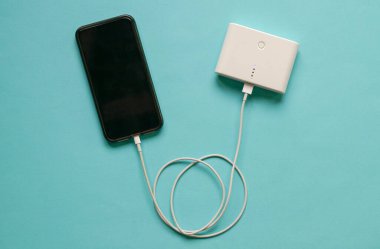 Cep telefonunun elektrik bankasından şarj olması. İzole edilmiş. Mavi arkaplanda.