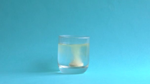 女人把一个冒着泡泡的橙色维生素C药片扔进一杯水里 自己溶化 蓝色背景 保持健康 建立强大的免疫系统概念 — 图库视频影像