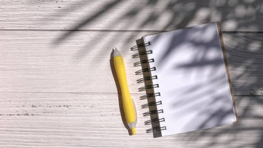 Not defteri ve kalem ahşap masanın üzerinde, palmiye yapraklarının gölgesi.