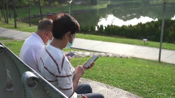 Casal Asiático Sênior Usando Máscara Facial Sentado Banco Parque Lendo — Vídeo de Stock