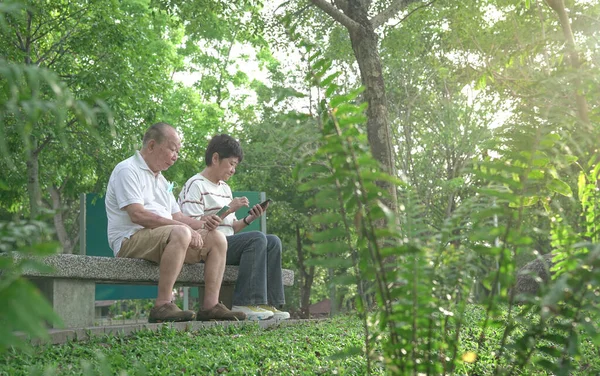 Senior Couple Sitting Bench Reading Phones Park Digital Lifestyle Retirees — Stock Photo, Image