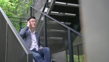 İş adamı merdivenlerde oturuyor, telefonu kulağında, sohbet ediyor ve gülümsüyor. Şehir ayarı, kopyalama alanı.