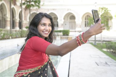 Güzel Hintli kadın gülümsüyor ve fotoğraf çekmek için kameralı telefonu kullanıyor..