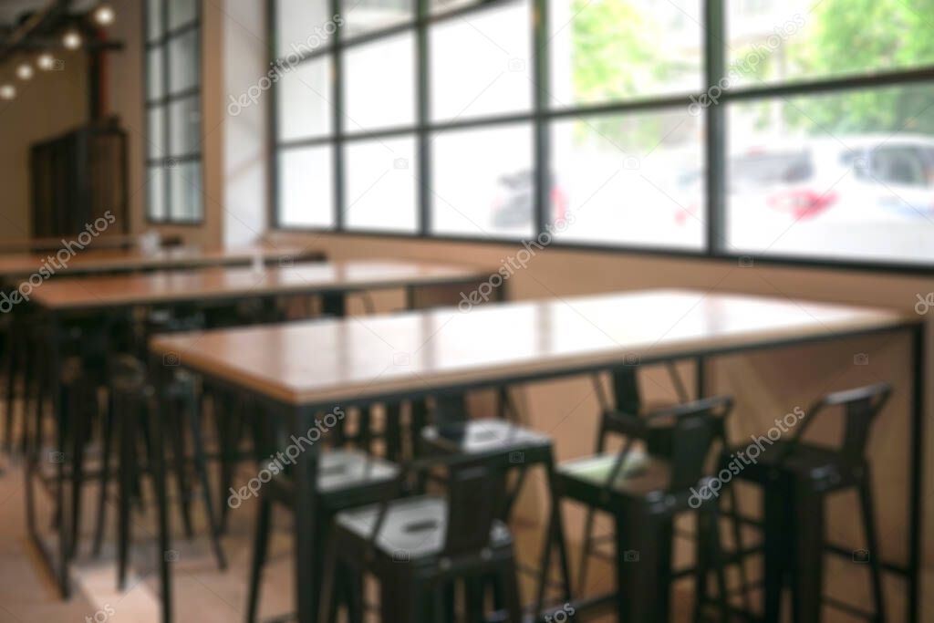 Empty cafetaria with wooden tables and high chairs, and windows with a view of outside. Defocused.