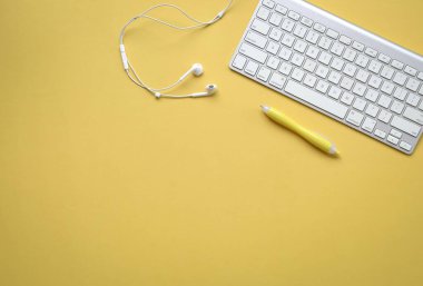 Bilgisayar klavyesi, kulaklığı ve sarı kalemi olan sarı ofis masası. Boşluğu kopyala.