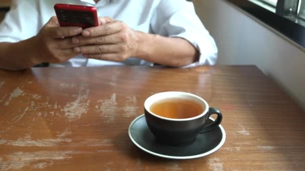 背景にテキストにスマートフォンを使用してマンの手 テーブルの上のお茶のカップに焦点を当てます 撃たれた — ストック動画