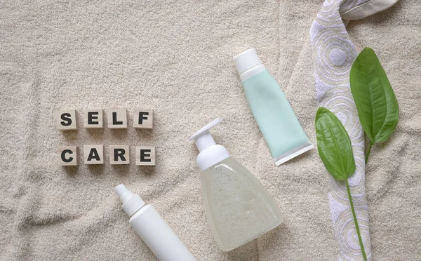 Self care word on wooden cubes, on top of towel with body and mind care products. Top view, copy space.