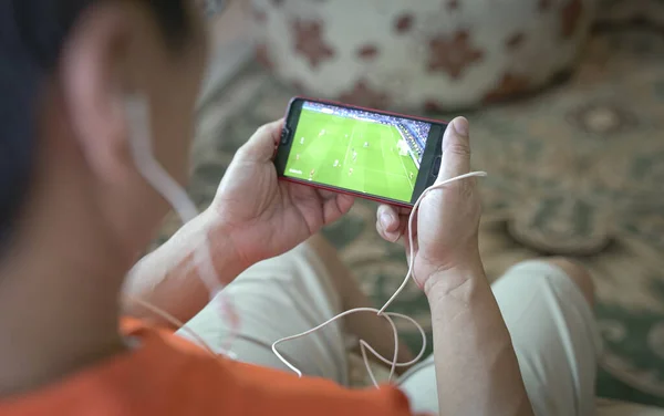Akıllı telefondan futbol ve spor kanallarını izleyen bir adam. Ev içi arkaplan.