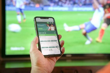 Televizyonda futbol maçı izleyip cep telefonuyla bahisçinin uygulamasına bahis oynuyorum. Yakın çekim..