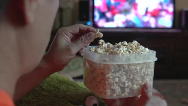 テレビでスポーツを見ながらポップコーンを食べるソファの上の男のバックビュー ビューを閉じる — ストック動画