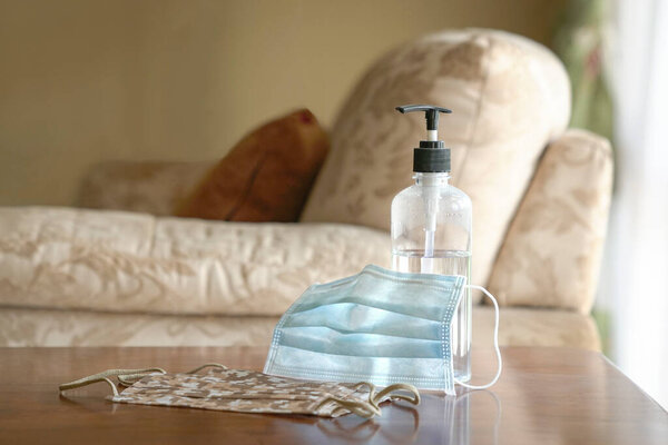 Hand sanitizer and face masks on table. Home interior background. Coronavirus prevention and protection.