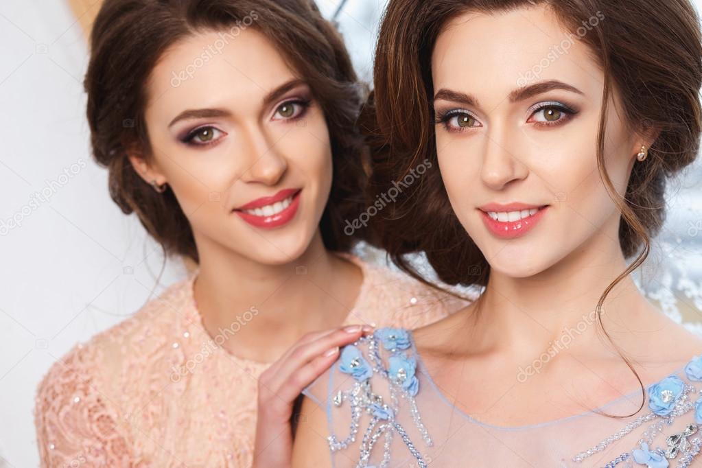 Close-up portrait of beautiful twins young women in luxury dresses, pastel colors. Beauty fashion portrait