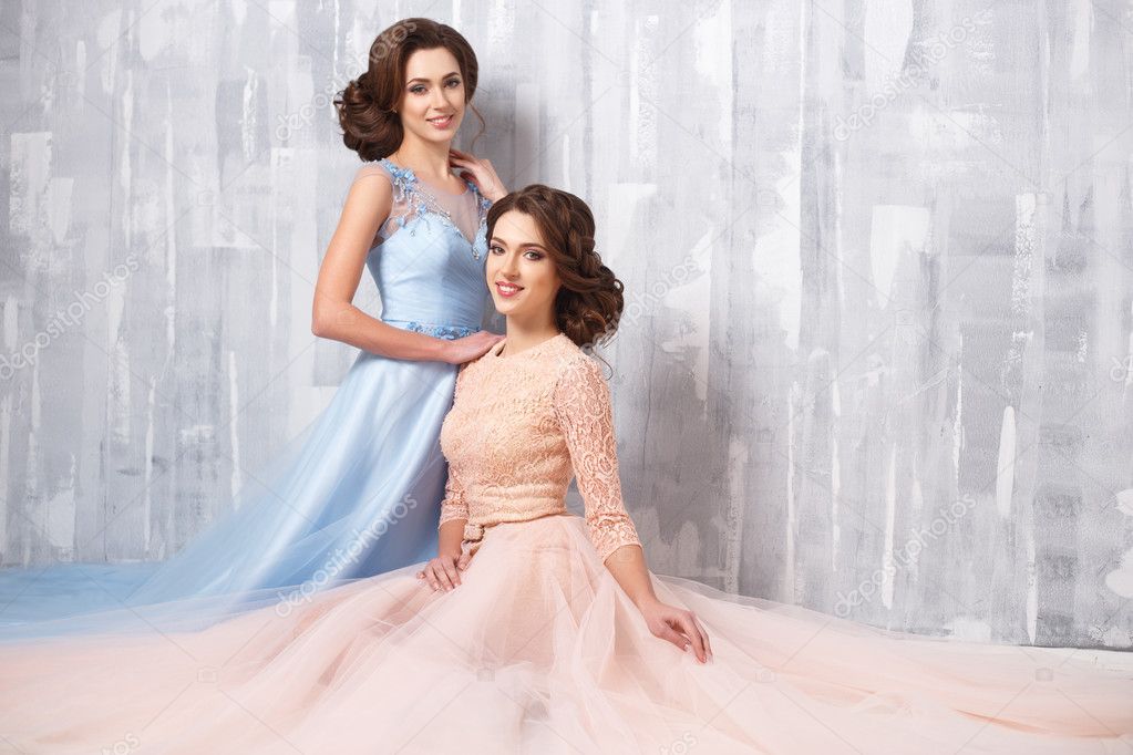 Two beautiful twins young women in luxury dresses, pastel colors. Beauty fashion portrait