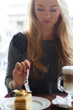 Kız, şehrin bulanık arka plan üzerinde bir kafede kek ve latte kahve fincan bir parça yemek