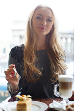 Kız, şehrin bulanık arka plan üzerinde bir kafede kek ve latte kahve fincan bir parça yemek