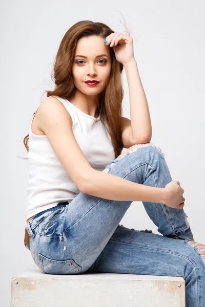 Close-up portrait of beautiful young woman with gorgeous hair and natural makeup sitting on a white cube. Fashion beauty photo, casual jeans style — Stock Fotó