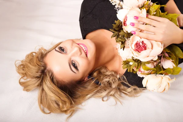 Nahaufnahme Porträt der schönen lockigen jungen Frau, die auf einem Bett liegt und einen Blumenstrauß hält. Schönheitsmodenporträt — Stockfoto