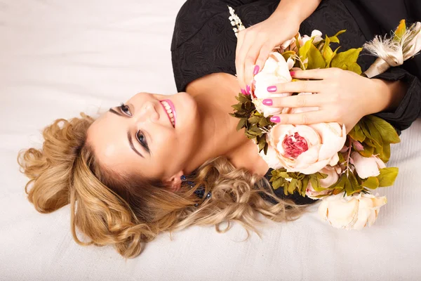 Nahaufnahme Porträt der schönen lockigen jungen Frau, die auf einem Bett liegt und einen Blumenstrauß hält. Schönheitsmodenporträt — Stockfoto