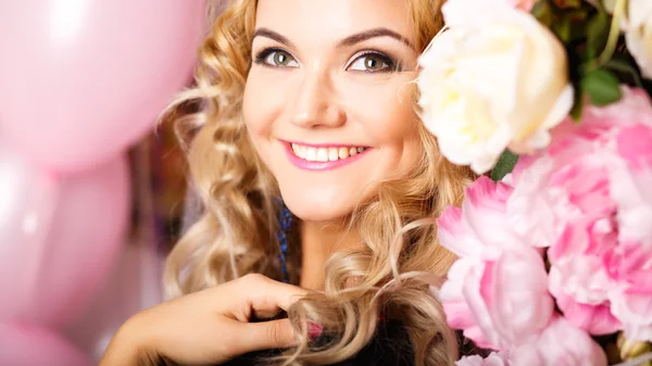 Close-up portrait of beautiful curly young woman in a room with many pink and white air balloons and flowers. Beauty fashion portrait
