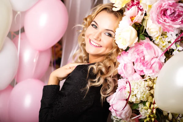 Retrato de cerca de una hermosa joven rizada en una habitación con muchos globos de aire y flores rosas y blancas. Retrato de moda de belleza — Foto de Stock