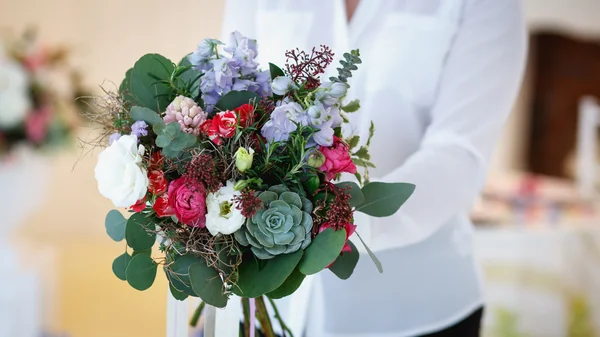 Jonge vrouw houdt een boeket die ze maakte. Decor en de samenstelling van de bloemen op een tafel. — Stockfoto