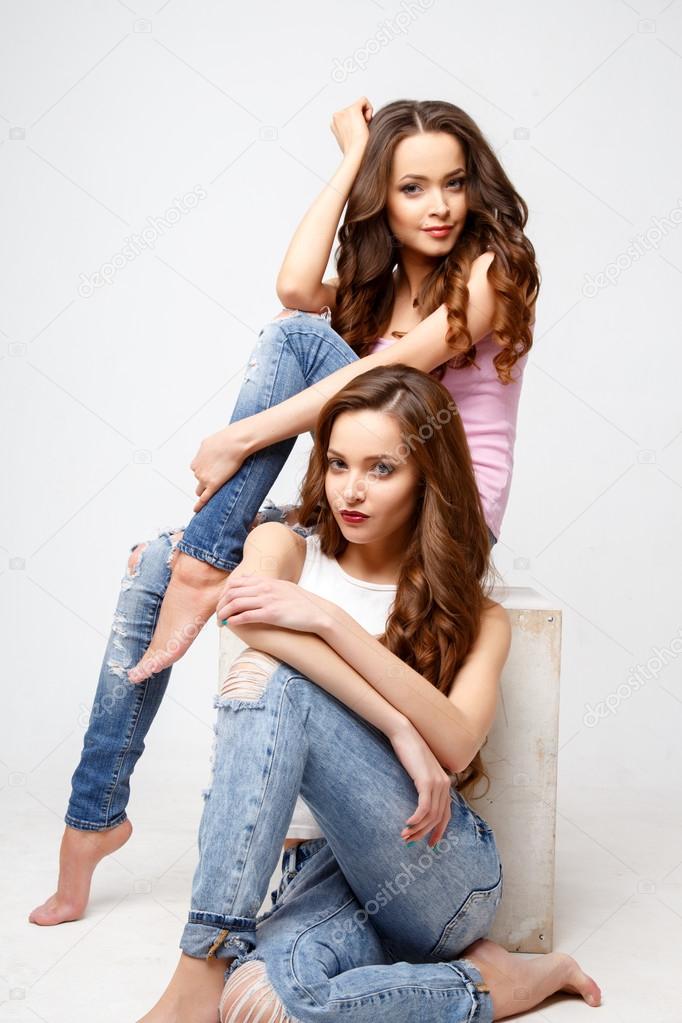 Beautiful twins young women in casual clothes over white background. Beauty fashion portrait, casual style
