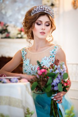 Bir buket çiçek ile bir tablo başına oturmuş bir lüks mavi elbiseli güzel genç bayan