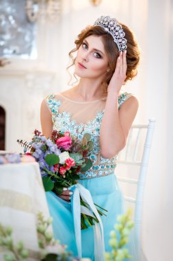 Bir buket çiçek ile bir tablo başına oturmuş bir lüks mavi elbiseli güzel genç bayan