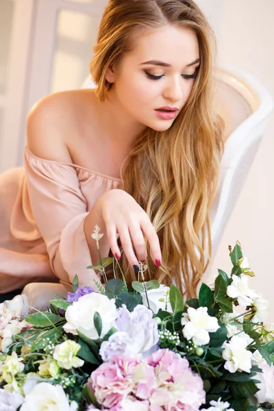 Junge blonde Frau umgeben von Blumen in einem hellen Raum. Zartes Porträt an einem Morgen — Stockfoto