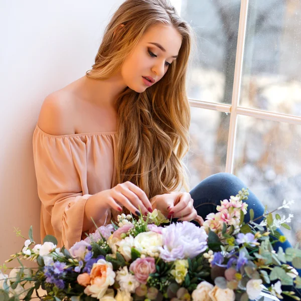 Mujer rubia joven con un ramo de flores sentado cerca de la ventana. Retrato tierno en una mañana — Foto de Stock