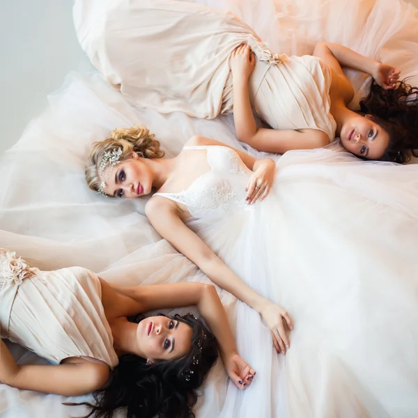 Beautiful blonde bride and pretty twins bridesmaids lying together on a floor — Stock fotografie