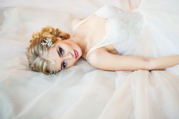 Schöne blonde Braut auf ihrem Hochzeitskleid liegend — Stockfoto