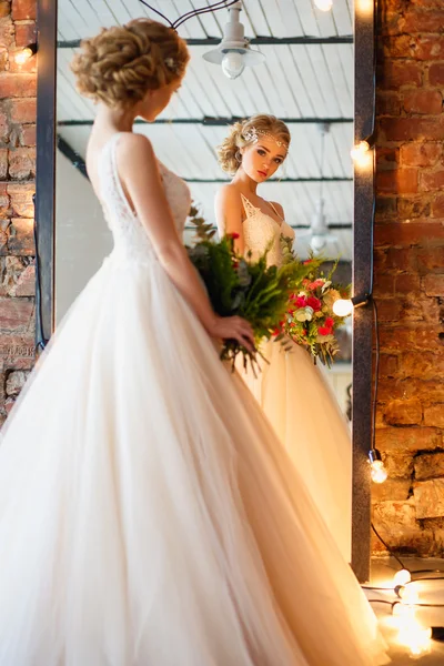 Hermosa novia rubia en magnífico vestido de lujo en un espacio loft con un espejo y guirnalda de lámparas. Boda moderna foto — Foto de Stock