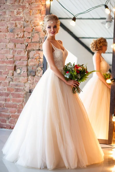 Belle mariée blonde dans une magnifique robe de luxe dans un espace loft avec un miroir et une guirlande de lampes. Photo de mariage moderne — Photo