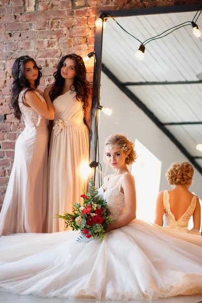 Gyönyörű szőke menyasszony luxus menyasszonyi ruha és szép ikrek koszorúslányok hasonló ruhák egy reggel egy tetőtéri térben egy tükör és Koszoru lámpák. Fashion modern esküvői fotó. — Stock Fotó