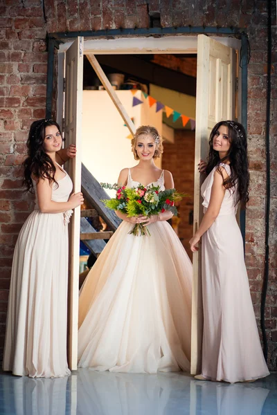 Bela noiva loira em vestido de noiva de luxo e gêmeas bonitas damas de honra em vestidos semelhantes em uma manhã em um espaço loft. Moda moderna casamento foto — Fotografia de Stock