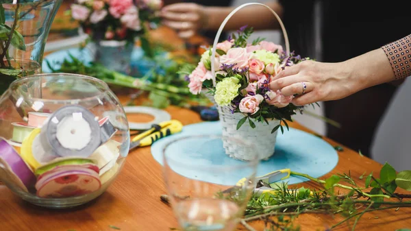 Taller floral - florista hace un ramo en una canasta. Estudiantes floristas trabajan juntos . — Foto de Stock