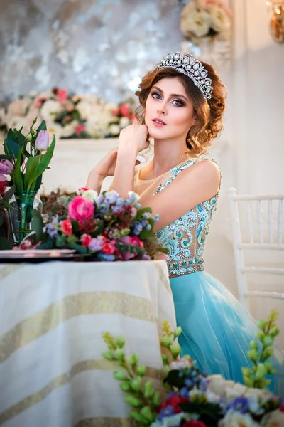 Bir buket çiçek ile bir tablo başına oturmuş bir lüks mavi elbiseli güzel genç bayan — Stok fotoğraf