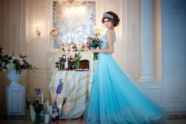 Menina bonita em um vestido azul de luxo em interior elegante com um buquê de flores — Fotografia de Stock