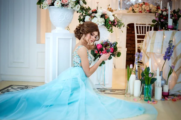 Красивая девушка в роскошном голубом платье в элегантном интерьере с букетом цветов — стоковое фото