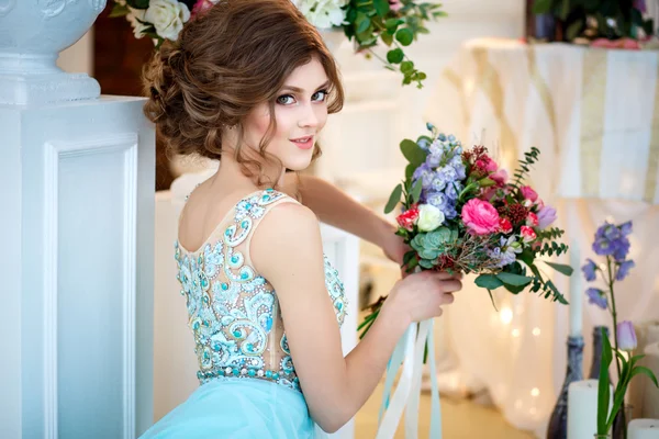 Menina bonita em um vestido azul de luxo em interior elegante com um buquê de flores — Fotografia de Stock