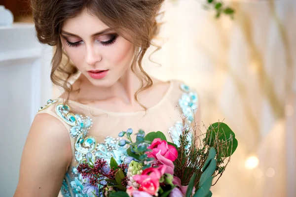 Menina bonita em um vestido azul de luxo em interior elegante com um buquê de flores — Fotografia de Stock