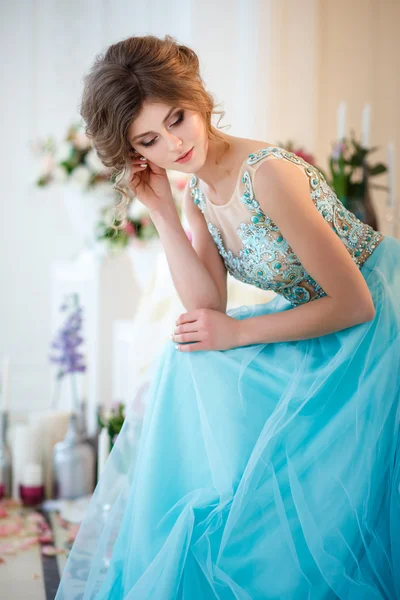 Schöne junge Dame in einem luxuriösen blauen Kleid in elegantem Interieur mit Blumen dekoriert — Stockfoto